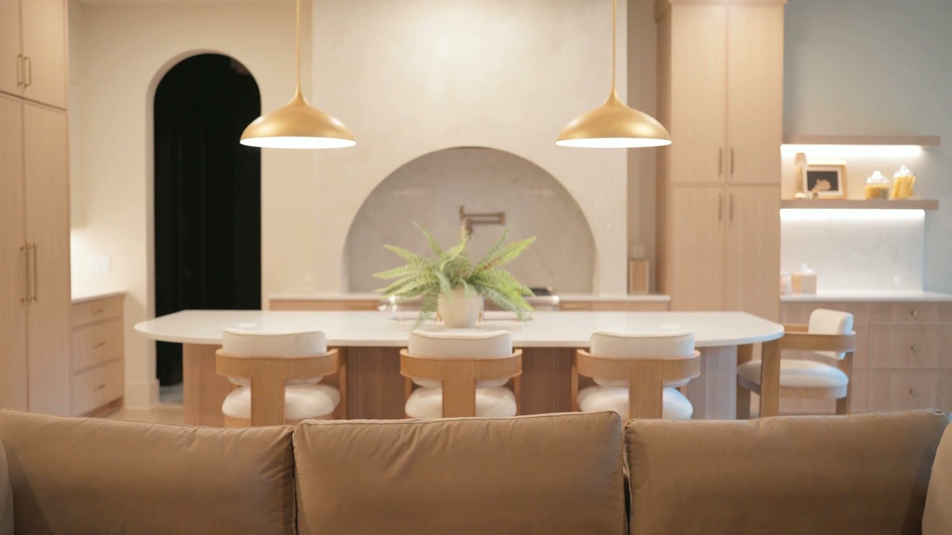 The kitchen and dining table under three brass pendants, arched range alcove beyond