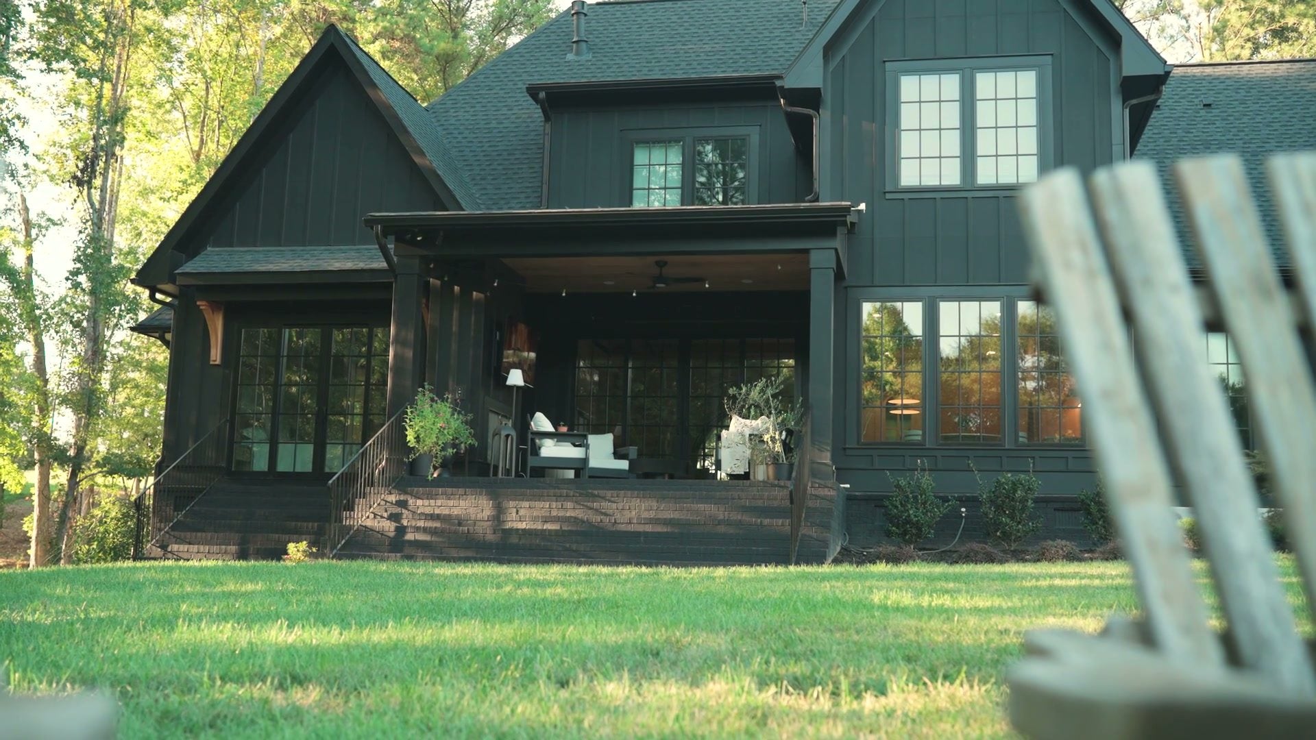 The back of the house across the lawn: the covered porch and two Adirondack chairs on the grass