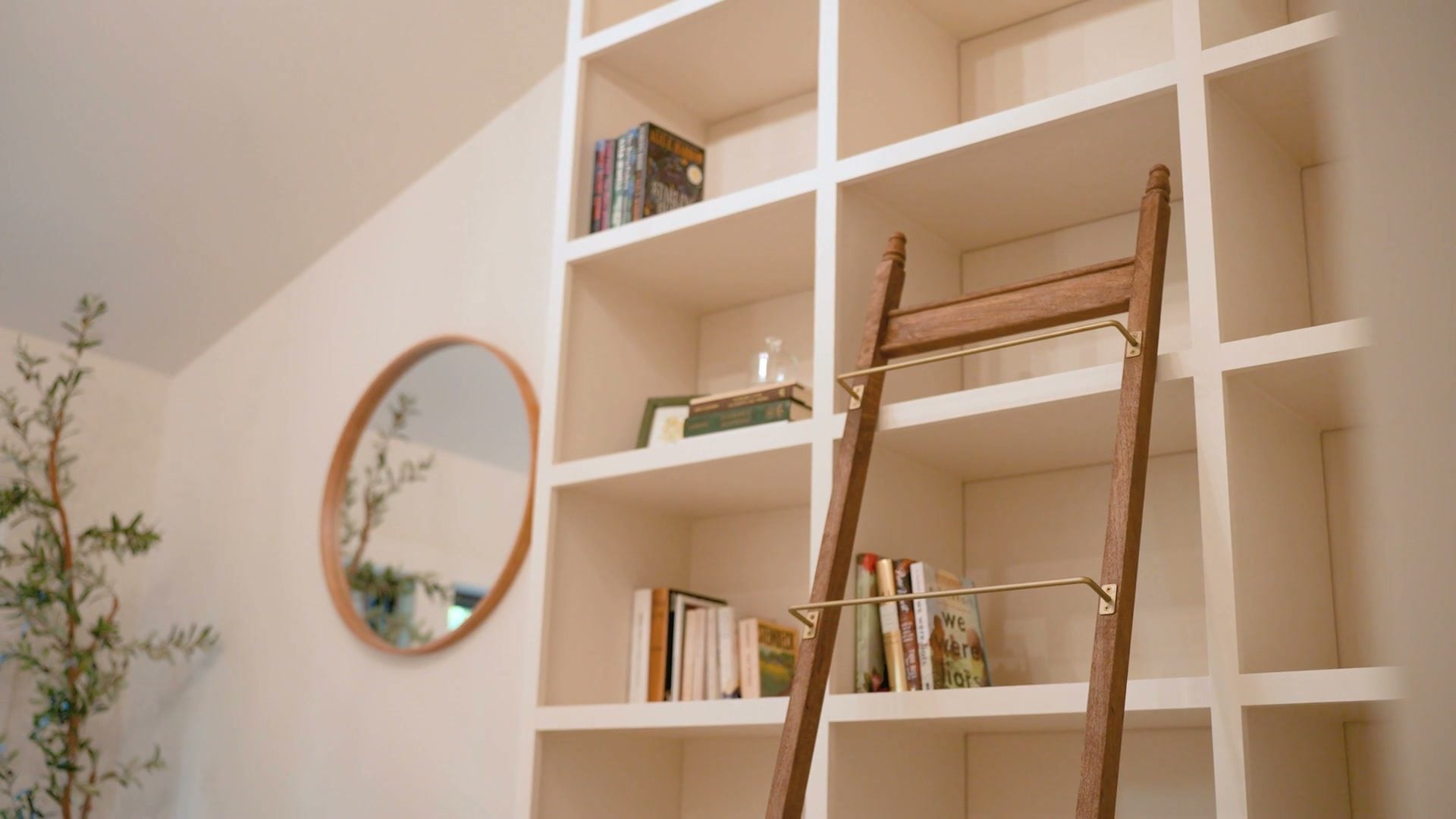 The library shelving with the rolling oak ladder and a round mirror beside it