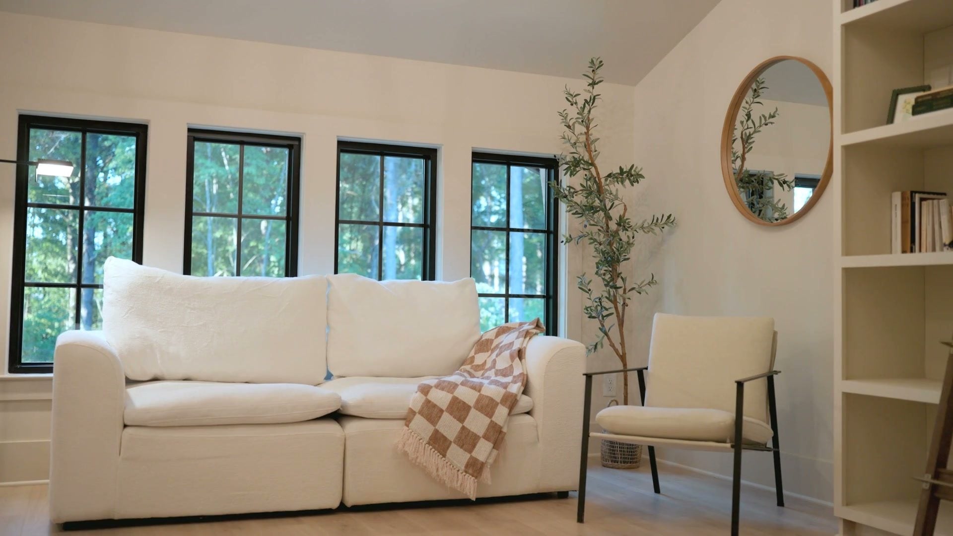 The living room: a white sofa under a brass chandelier, steel-framed windows and a round mirror on the wall