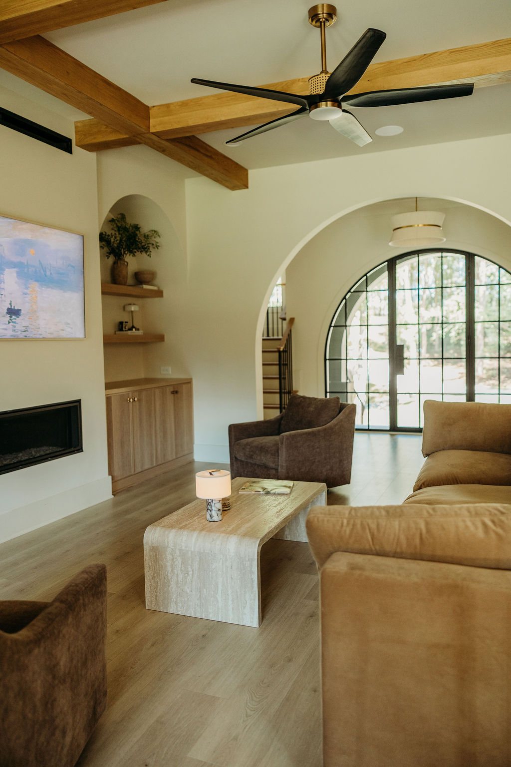 The sitting area by the fireplace: tan sofas, oak beams and an arched window