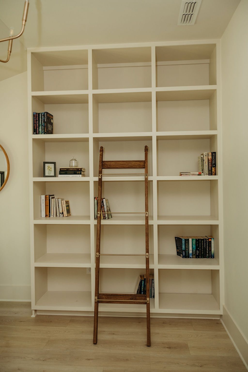 The library wall: white shelving with books and the rolling oak ladder